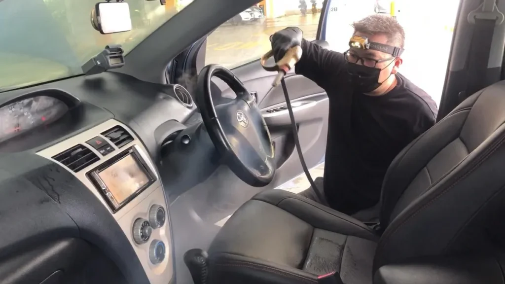 Detallista con cubrebocas aplicando vapor en tablero y asiento