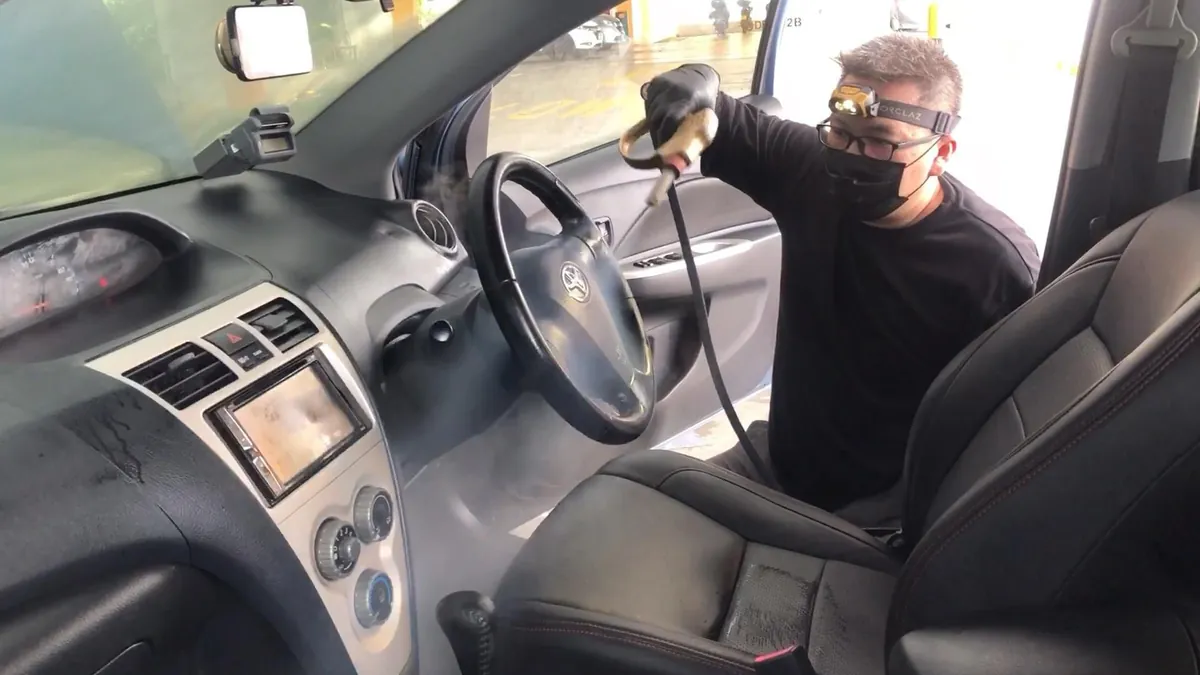 Detallista con cubrebocas aplicando vapor en tablero y asiento: lavado de asientos de autos a vapor