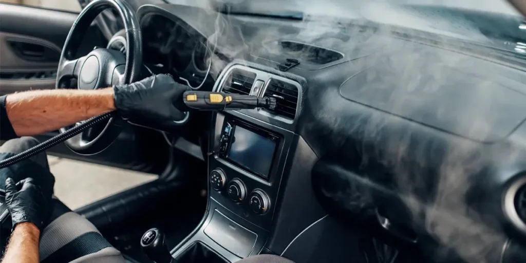 Detallista con guantes aplicando vapor en ventilas y tablero de un auto