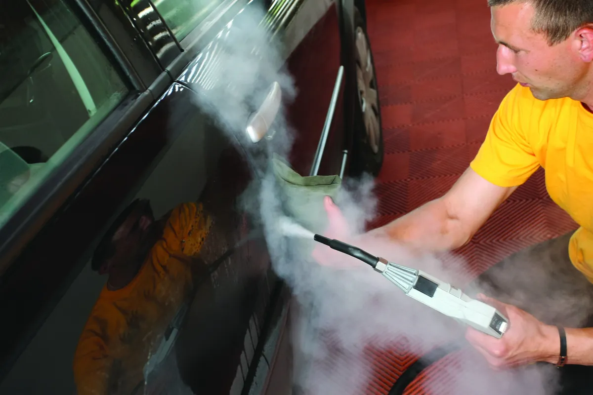 Vapor sobre la ventana y la carrocería de un auto negro: autolavado a vapor